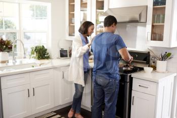 Back view of young couple standing in the kitchen preparing food together