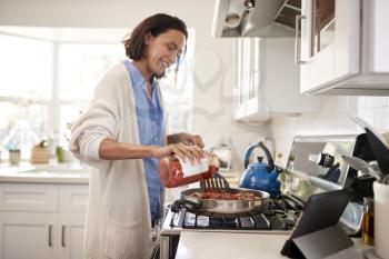 Young mixed race adult woman standing in the kitchen cooking on the hob, adding a sauce to the frying pan, close up