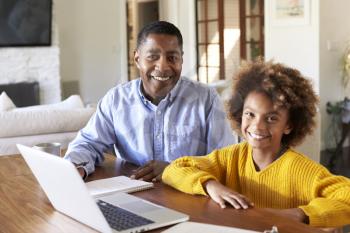 Pre-teen black girl and her male home tutor sitting at a table in the dining room smiling to camera, close up