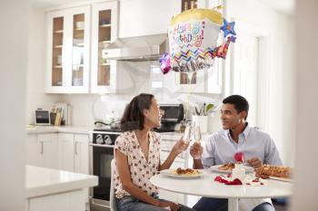 Young couple sitting at the table in their kitchen making a toast while eating a romantic birthday meal together, selective focus