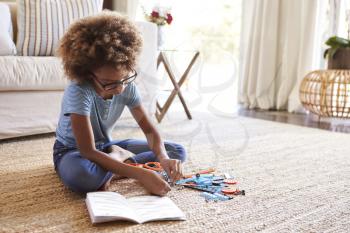 Pre-teen girl sitting on the floor in the living room reading instructions and constructing a model, close up