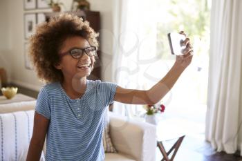 Pre-teen girl taking a selfie photo standing in the living room laughing, close up, focus on foreground
