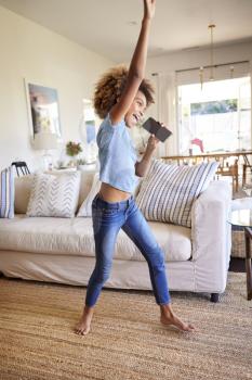Pre-teen black girl dancing and singing in the living room at home using her phone as a microphone, side view, full length, vertical