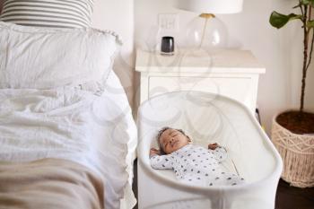 Three month old baby asleep in his cot beside the bed in his mother’s bedroom
