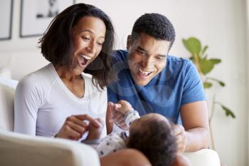 Happy mixed race young adult parents playing with their three month old baby son, lying on his mother’s knee, selective focus