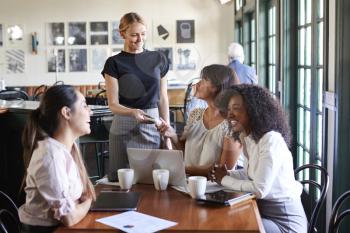 Businesswomen Paying Bill At Meeting Around Table In Coffee Shop