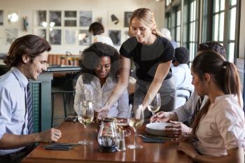 Waitress Serving Meal To Business Colleagues Sitting Around Restaurant Table