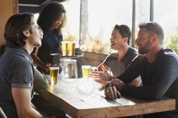 Waitress Serving Drinks To Group Of Male Friends Meeting In Sports Bar