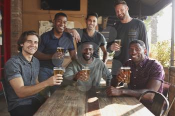 Group Of Male Friends Meeting In Sports Bar Making Toast Together At Camera