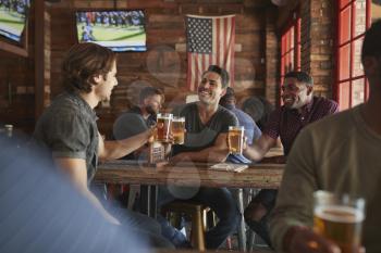 Group Of Male Friends Meeting And Drinking Beer In Sports Bar Together