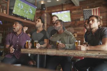 Group Of Male Friends Watching Game On Screen In Sports Bar