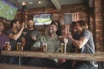 Group Of Friends Watching Game On Screen In Sports Bar