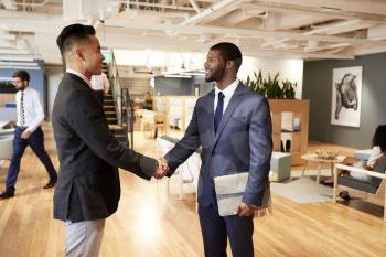 Two Businessmen Meeting And Shaking Hands In Modern Open Plan Office
