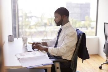 Businessman Sitting At Desk Working On Laptop In Modern Office
