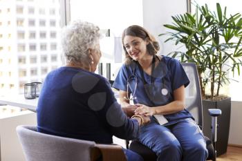 Nurse Wearing Scrubs In Office Reassuring Senior Female Patient And Holding Her Hands