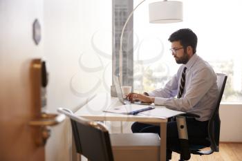 Businessman Sitting At Desk Working On Laptop In Modern Office