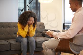 Unhappy Woman Sitting On Couch Meeting With Male Counsellor In Office