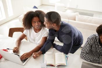 Teenage black girl doing homework with help from her dad, looking at each other, elevated view