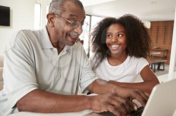 Smiling teenage black girl sitting at home helping her grandfather use a laptop computer,close up