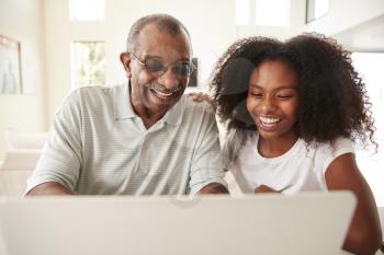 Teenage black girl helping her grandfather use a laptop computer, front view, close up