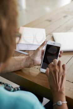Over shoulder view of senior black woman sitting at table using smartphone, close up, vertical