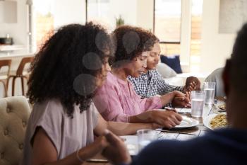 Close up of black family sitting at dinner table holding hands and saying grace before meal