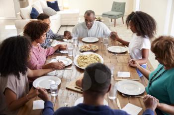 Three generation black family holding hands and saying grace at table before dinner,elevated view