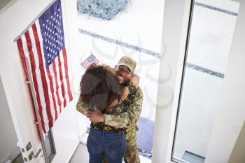 Elevated view of returning black male soldier embracing his wife in the doorway of their home