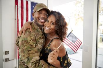 Millennial black soldier and wife embracing at home and smiling to camera,waving flag, close up