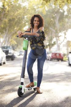 Millennial black woman standing in the street leaning on an electric scooter,full length, close up