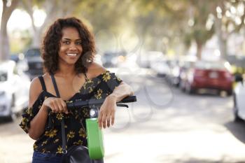 Close up of millennial black woman leaning on an electric scooter in the street, smiling to camera