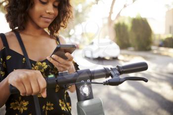 Millennial black woman standing on an electric scooter using smartphone,close up