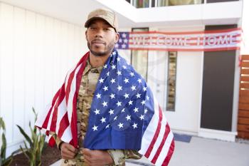 Millennial black soldier with US flag draped over his shoulders, looking to camera, close up