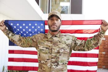 Millennial black soldier standing outside modern building holding US flag, looking to camera, close up