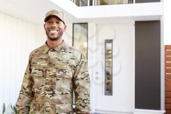 Millennial soldier in camouflage uniform standing outside modern house smiling to camera, close up