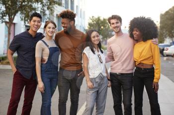 Six millennial hipster friends standing in a city street smiling to camera, three quarter length