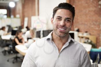 Portrait Of Mature Businessman In Modern Open Plan Office With Business Team Working In Background