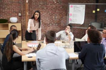 Young Businesswoman Standing And Leading Office Meeting Around Table