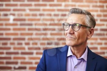 Mature Businessman Standing Against Brick Wall In Modern Office