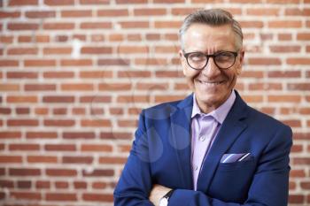 Portrait Of Smiling Mature Businessman Standing Against Brick Wall In Modern Office
