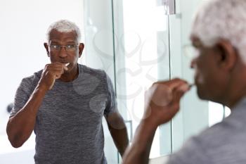 Senior Man Looking At Reflection In Bathroom Mirror Wearing Pajamas Brushing Teeth