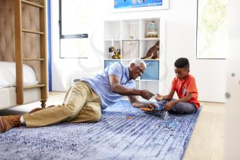 Grandfather With Grandson Lying On Rug At Home Building Robotic Model Together