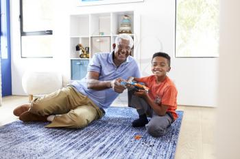 Portrait Of Grandfather With Grandson Lying On Rug At Home Building Robotic Model Together