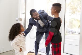 Children Greeting And Hugging Working Businessman Father As He Returns Home From Work