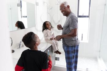 Grandfather In Bathroom Wearing Pajamas Brushing Teeth With Grandchildren