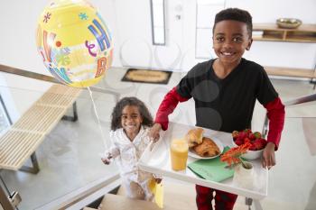 Portrait Of Children Bringing Parents Breakfast In Bed On Tray With Balloon To Celebrate Birthday