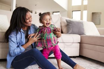 Mother Playing With Baby Daughter Sitting On Floor Of Lounge At Home
