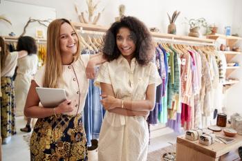 Portrait Of Two Female Sales Assistants With Digital Tablet Working In Clothing And Gift Store