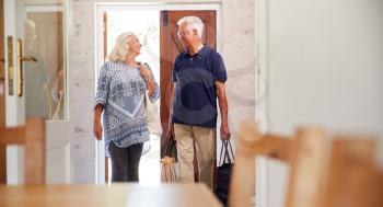 Senior Couple Returning Home From Shopping Trip Carrying Grocery Bags Through Kitchen