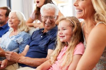 Multi-Generation Family Sitting On Sofa At Home Watching Movie Together